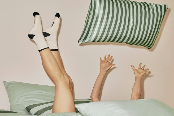 how to choose a pillow blog post image. Girl throwing striped green and white pillow up in the air.